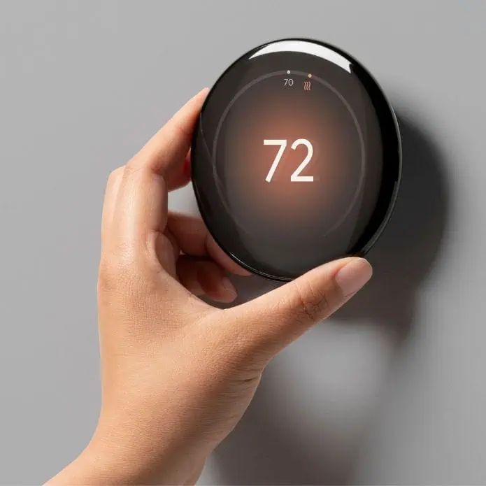 Nest Learning Thermostat 4th Gen with a white hand touching the edges of a circular screen display. With a black background fading into an orange centre the number 72 is written in white in the middle of the glass screen display